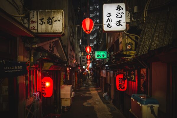 A narrow alleyway in Tokyo at night with glowing red lanterns and illuminated signs
