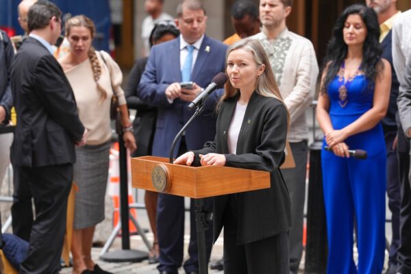 Woman speaks at podium with crowd behind her