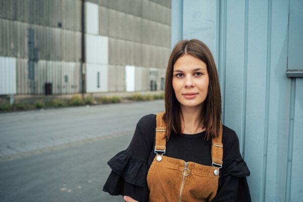 woman in black long sleeve shirt and brown leather shoulder bag standing beside blue wall during