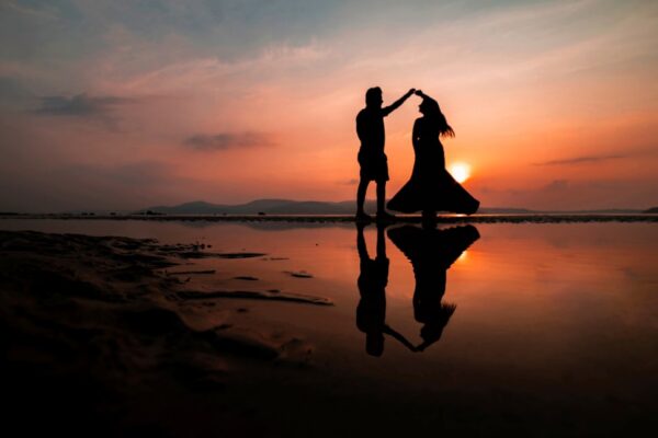 A silhouette of two people dancing on a beach at golden hour