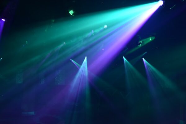 Bright teal and purple spotlights cutting through a dark hazy nightclub atmosphere